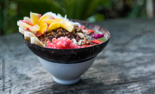 smoothie bowl in a coconut shell plate with with strawberries, chia seeds, banana, granola, flower on wooden background