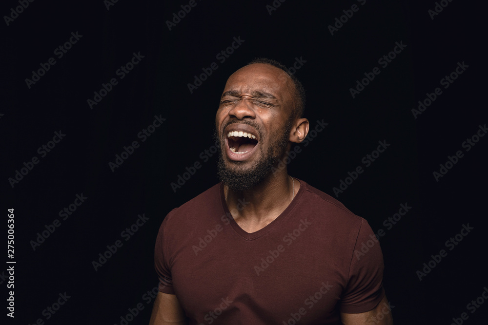 Fototapeta premium Close up portrait of young man isolated on black studio background. Photoshot of real emotions of male model. Crying, sad, dreary and hopeless. Facial expression, human emotions concept.