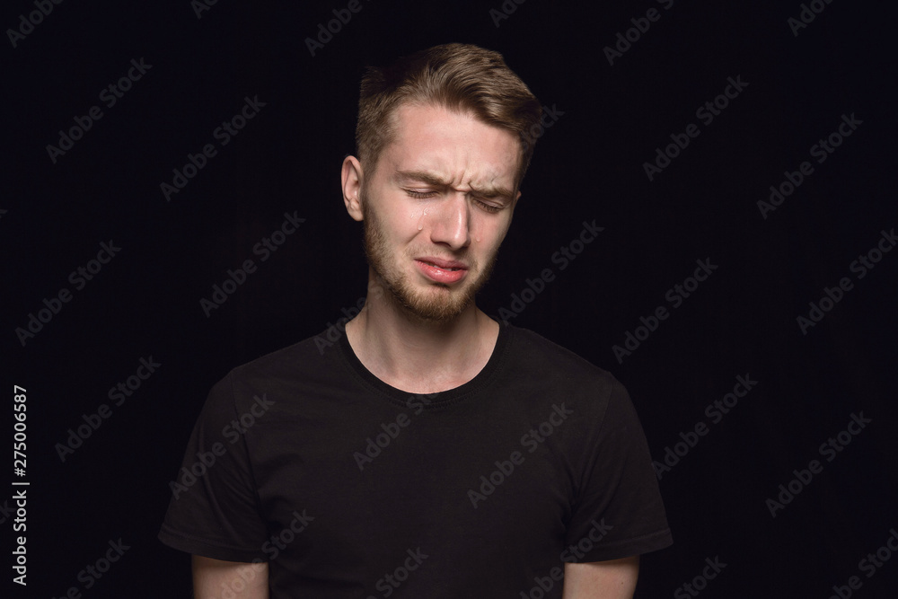 Close up portrait of young man isolated on black studio background. Photoshot of real emotions of male model. Crying with closed eyes, sad and hopeless. Facial expression, human emotions concept.