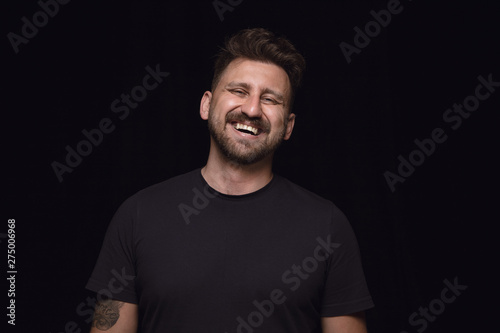 Close up portrait of young man isolated on black studio background. Photoshot of real emotions of male model. Crying throught laughting and smiling. Facial expression, human emotions concept.