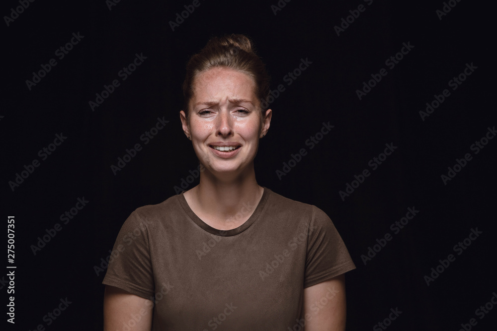 Close up portrait of young woman isolated on black studio background. Photoshot of real emotions of female model. Crying, sad, dreary and hopeless. Facial expression, human emotions concept.