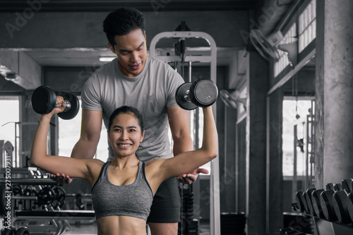 фотографія male trainer training female working out with dumbbells wieght lifting in gym