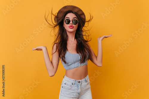 Lovable tanned girl in trendy summer attire dancing in studio on photoshoot. Indoor photo of fascinating brunette female model in blue tank-top and brown hat.
