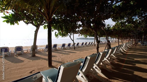 Row of deck chairs under tropical trees in the morning beach resort. Sunise. Nusa Dua sandy beach, Bali, Indonesia photo