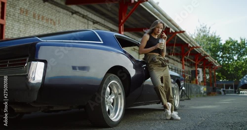 Beautiful Caucasian female posing with an old classic retro muscle car. Automotive lifestyle. 4K UHD RAW graded footage