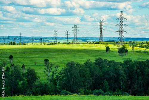 High voltage transmission towers on green grassland at sunny summer day  
