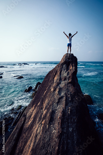 Successful young woman outstretched arms on seaside rock cliff edge