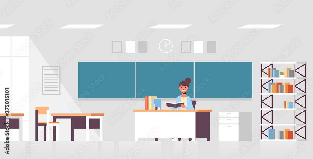 smiling teacher sitting at desk woman checking students copybook in front of green chalk board education concept modern classroom interior flat full length horizontal
