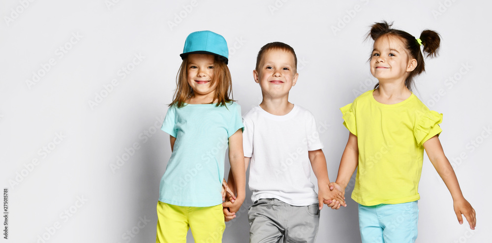 Obraz premium Studio portrait of children on a light background: full body shot of three children in bright clothes, two girls and one boy. Triplets, brother and sisters.