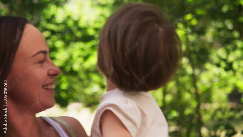 Happy mother hugs adorable little daughter and whirls with her in sunny park Happy mother hugs adorable little daughter and whirls with her in sunny park