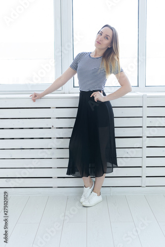Youth, style and people concept - young woman on black skirt and sneakers standing near the window