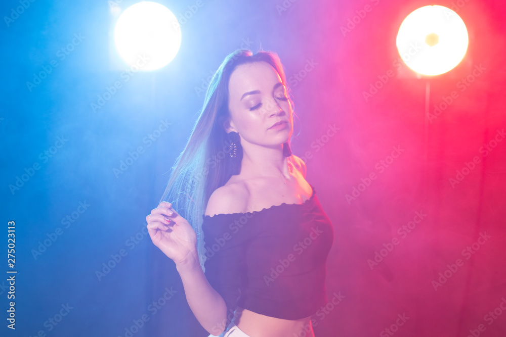 Nightlife and club concept - young woman dancing in the dark under the lights