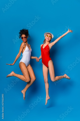 Two happy girlfriends in swimsuits jumping in air