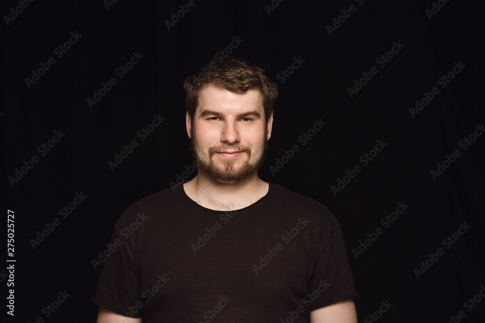 Close up portrait of young man isolated on black studio background. Photoshot of real emotions of male model. Smiling, feeling happy. Facial expression, pure and clear human emotions concept.