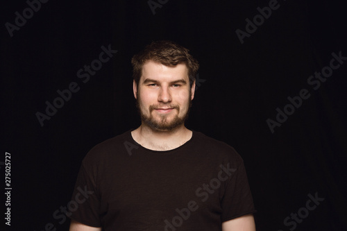 Close up portrait of young man isolated on black studio background. Photoshot of real emotions of male model. Smiling, feeling happy. Facial expression, pure and clear human emotions concept.