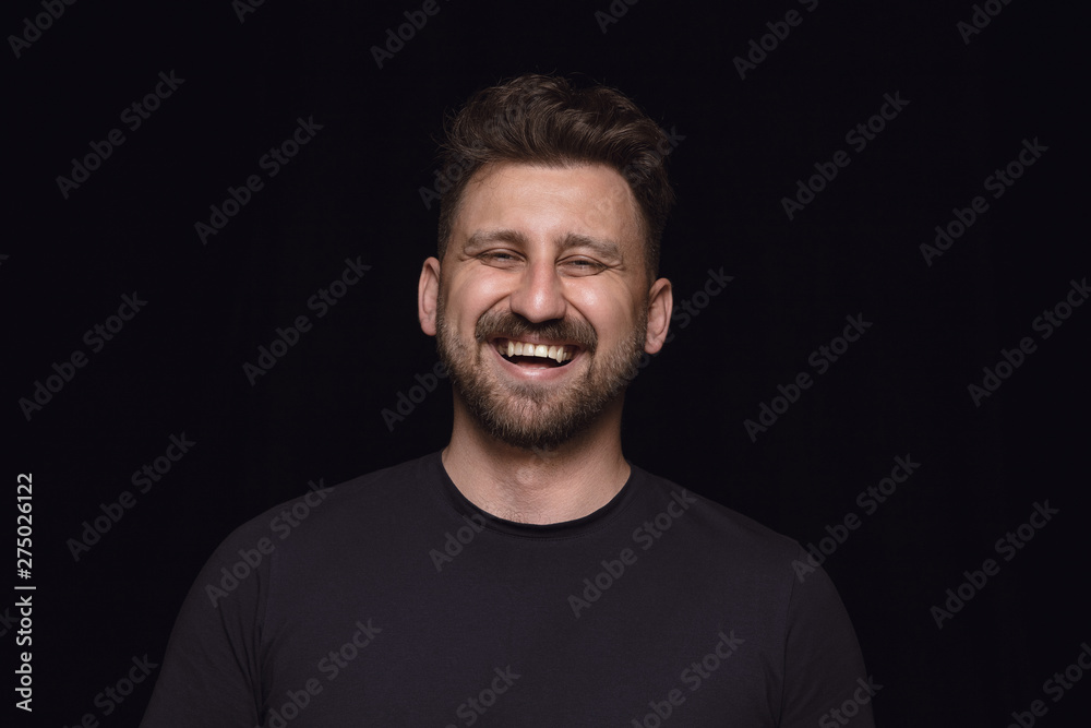 Close up portrait of young man isolated on black studio background. Photoshot of real emotions of male model. Smiling, feeling crazy happy, laughting. Facial expression, human emotions concept.