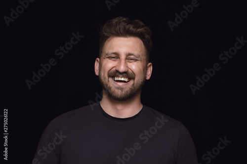 Close up portrait of young man isolated on black studio background. Photoshot of real emotions of male model. Smiling, feeling crazy happy, laughting. Facial expression, human emotions concept.