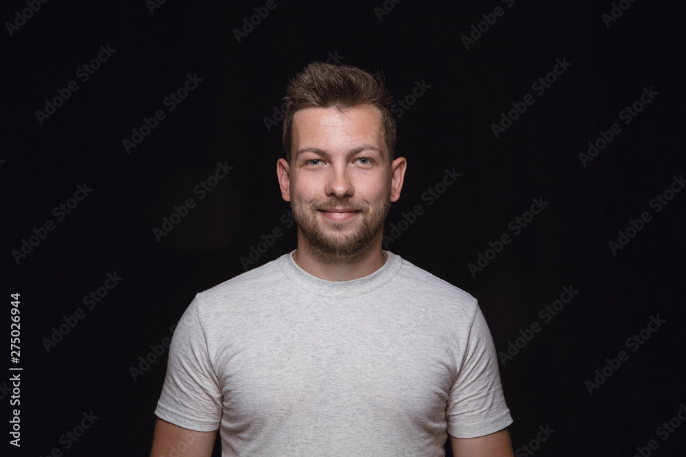 Close up portrait of young man isolated on black studio background. Photoshot of real emotions of male model. Smiling, feeling happy. Facial expression, pure and clear human emotions concept.