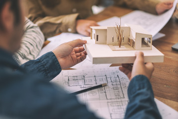 Group of an architect working and discussing about an architecture model together with shop drawing paper on table in office