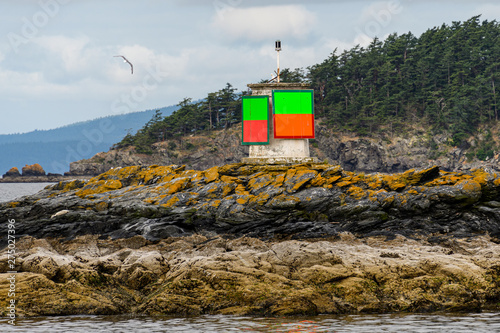 Close up of green and orange navigation marker on a rock in the Salish Sea, forested island and cloudy sky in background, San Juan Islands photo