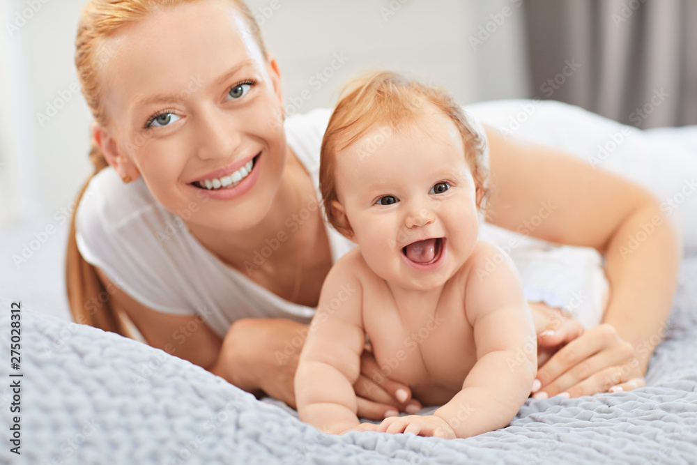 Mother and baby laugh lying on the bed. Mother and baby laugh lying on the bed.