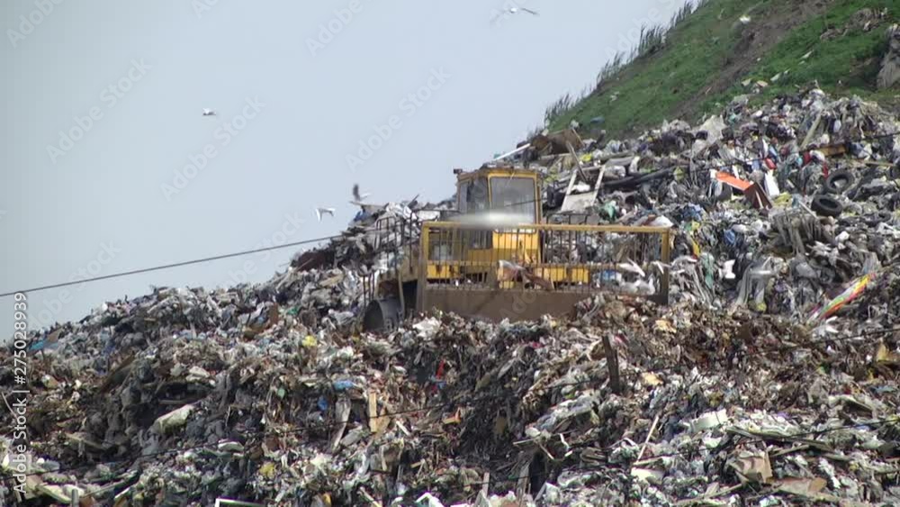 huge tractor with a front end loader and metal wheels is used to move trash in a city dump. huge tractor with a front end loader and metal wheels is used to move trash in a city dump.