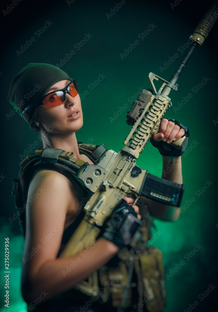 Obraz premium the girl in military special clothes posing with a gun in his hands on a dark background in the haze
