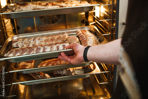 Smoked meat products in the oven smokehouse. A man holding a tray of smoked meat products