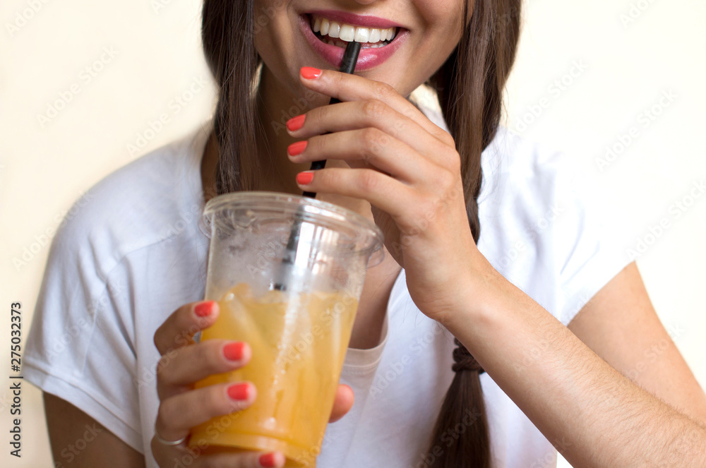 young woman in white shirt holding a plastic cup with an ised orange juice and smiling young woman in white shirt holding a plastic cup with an ised orange juice and smiling