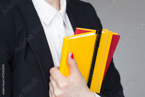 young woman in white shirt and black suit holding yellow and red note pads and black pen in her hands © MashaB