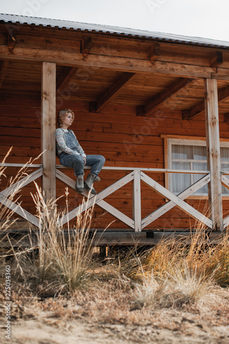 young blonde girl in overalls sits on the porch of a farmhouse