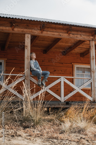 young blonde girl in overalls sits on the porch of a farmhouse