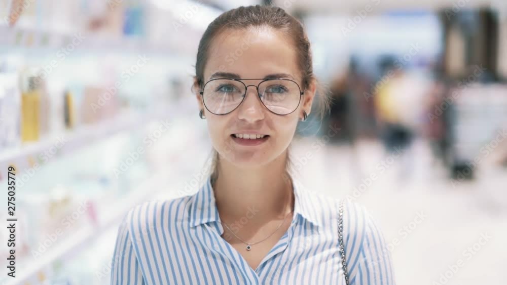 Portrait of girl glasses at cosmetic store smiles, looks at camera, slow motion Portrait of girl glasses at cosmetic store smiles, looks at camera, slow motion