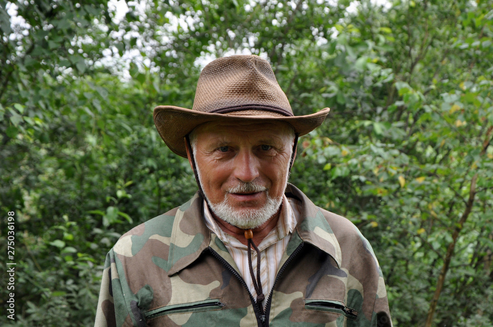 Middle aged traveler. Portrait of a handsome adult man with a gray beard and hat in camouflage clothing.