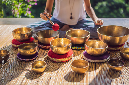 Woman playing on Tibetan singing bowl while sitting on yoga mat against a waterfall. Vintage tonned. Beautiful girl with mala beads meditating photo