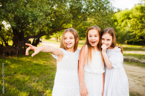 Three girls in white dresses walk in nature in the summer. Children's pastime during the summer holidays.