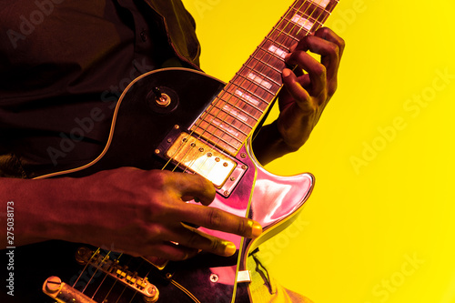 Photography Young african-american musician playing the guitar like a rockstar on yellow background in neon light