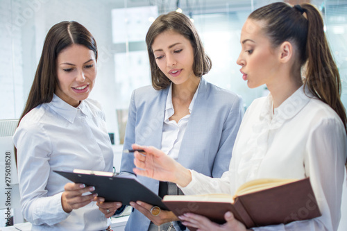 Group of three business women discussing document on meeting in modern office.