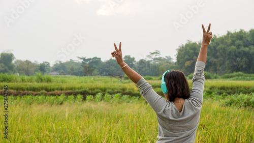 Woman throwing up peace sign as she listens to music while walking through countryside.