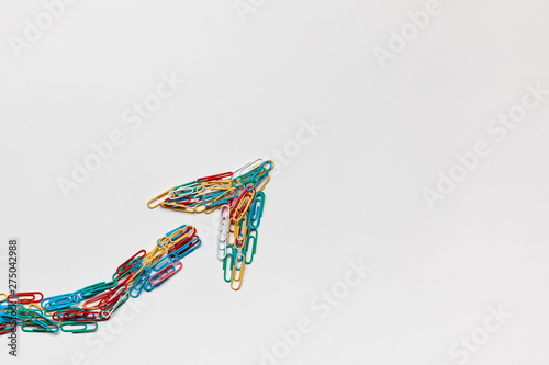 An arrow made from paperclips pointing upwards on a white background  shot from above.