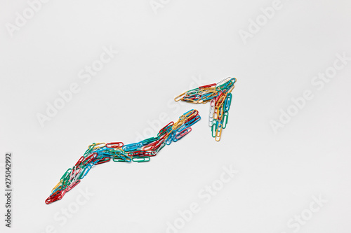 An arrow made from paperclips pointing upwards on a white background, shot from above.