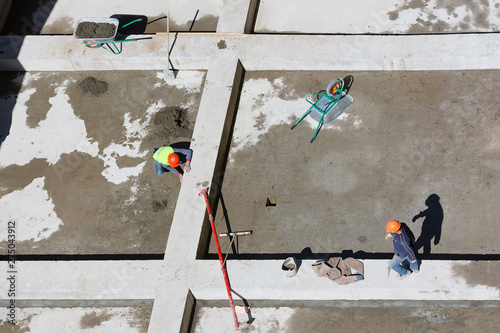 Uniformed workers clean sand on a construction site, top view.