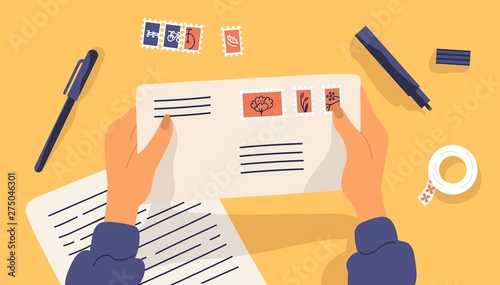 Hands holding envelope with stamps surrounded by stationery. Top view on table surface. Sending written letter or correspondence through postal service. Flat cartoon colorful vector illustration. photo