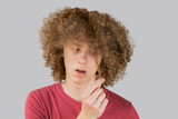portrait of a young curly european man frightened looks at his long hair. holds a curl of hair with his fingers. very lush male guy hair. curling hair for men. isolated on gray background