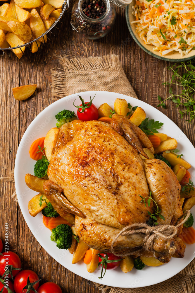 Roast chicken whole. Served on a plate with vegetables and baked potatoes.