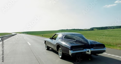 TRACKING Old classic vintage 70s muscle car driving thorough rural landscape. 4K UHD RAW graded footage