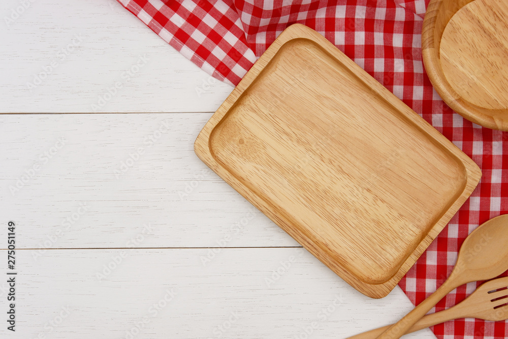 Empty rectangle wooden plate with spoon, fork and red gingham tablecloth on white wooden table. Top view image with copy space.