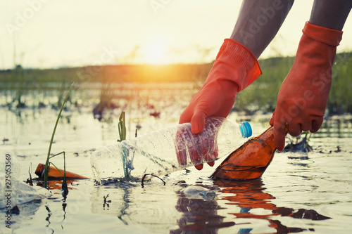 woman hand picking up garbage plastic for cleaning at river with sunset photo