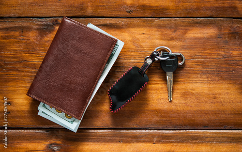 leather wallet and car key on wood table with dollar bills