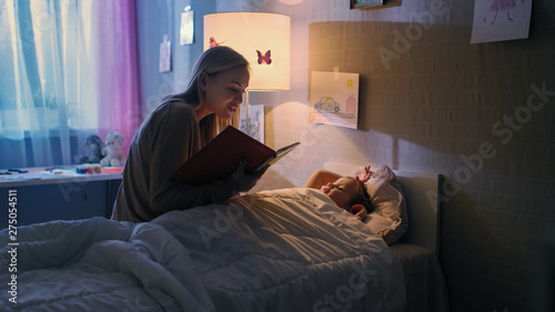 Foto Young Loving Mother Reads Bedtime Stories to Her Little Beautiful Daughter who Goes to Sleep in Her Bed
